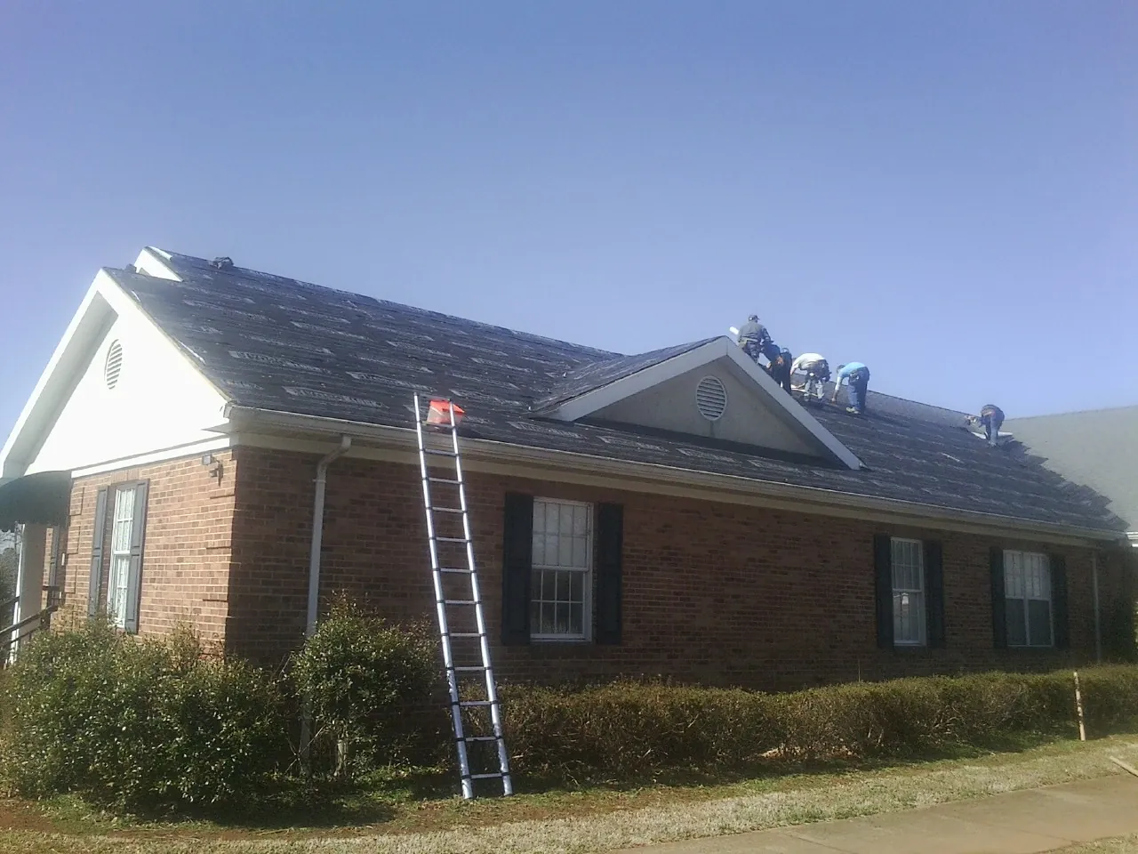 Crew tearing shingles off a brick ranch roof with a ladder set — Metal Roof Repair work by our crew in Orangeburg
