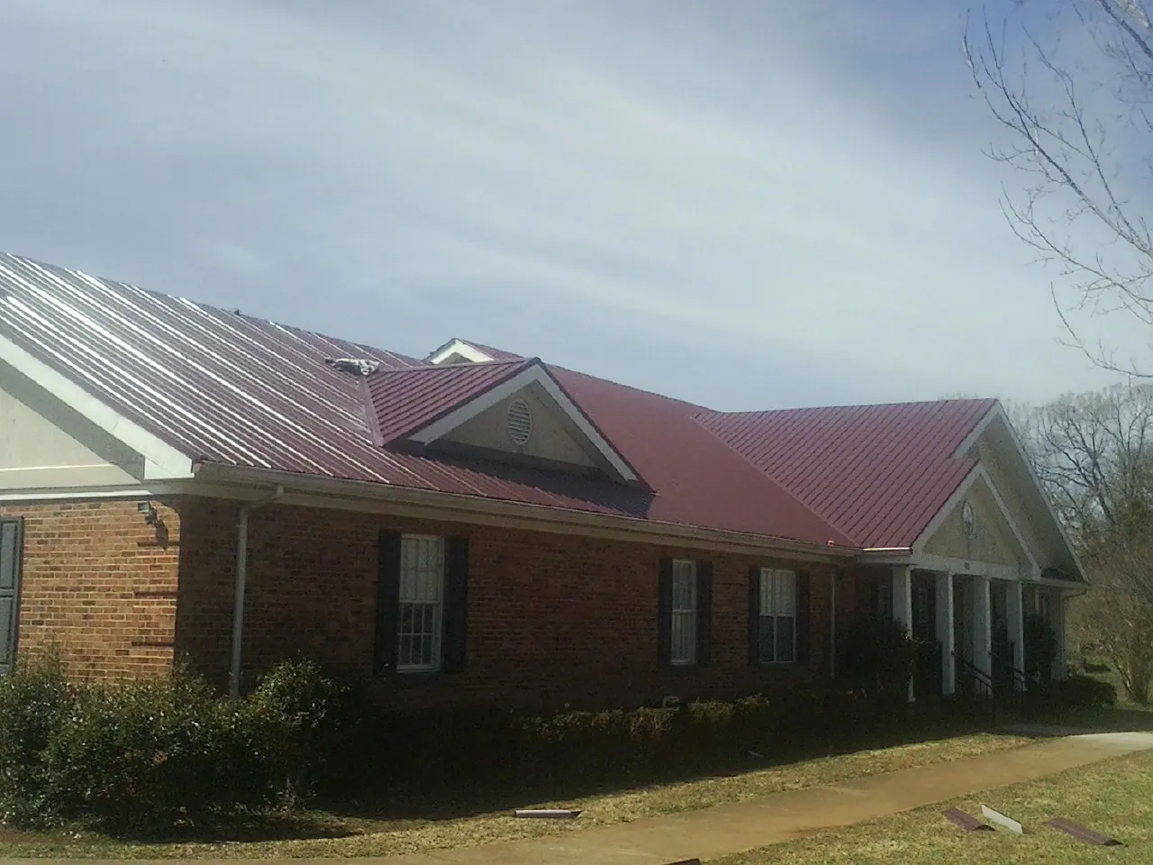 Red metal roof with gabled entries on a long brick building, from a Hail Damage Roof Repair job in Orangeburg