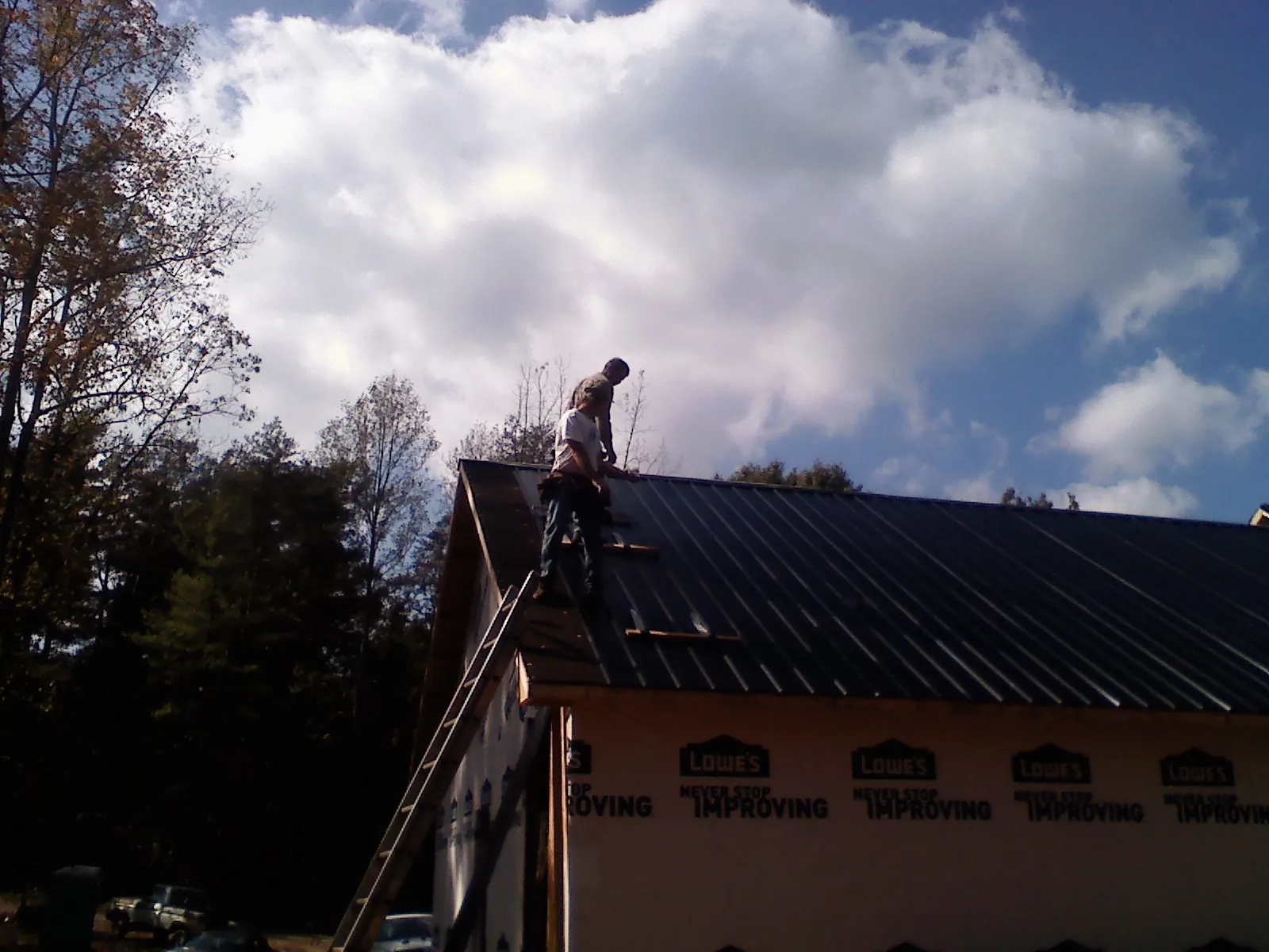 Roofer fastening dark metal panels high against a cloudy sky, from a Roof Inspection job in Orangeburg