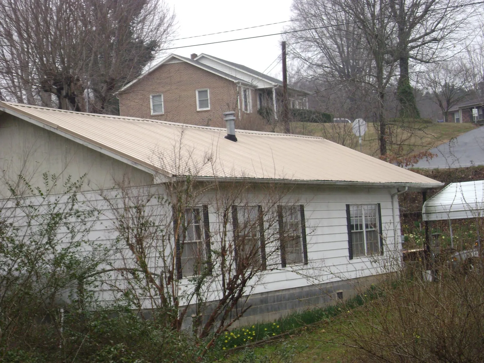 Tan metal roof on a white sided house set into a hillside — Commercial Roofing by Roofing Brothers in Orangeburg